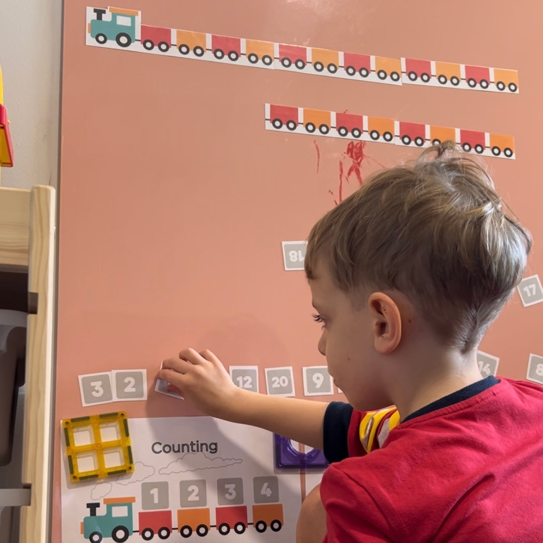 A pretty whiteboard that is actually a beautiful peach colour, being played with by a boy. The boy is using the magnets to learn about counting.