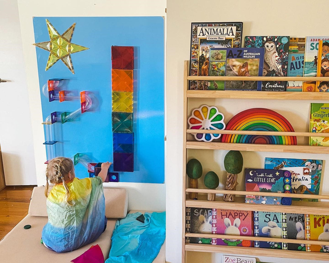 A vibrant blue whiteboard is being used as a canvas to play with Magnetic tiles. The pretty whiteboard is highly magnetic receptive, and has a magnetic tile ball run on it.